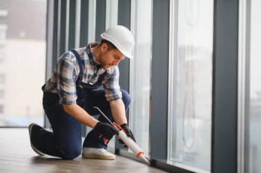 Modern bir binadaki pencere çerçevelerine hava geçirmez yalıtım ve enerji verimliliği sağlayan bir inşaat işçisi.