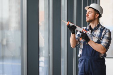 İnşaat işçisi, bir ofis binasının pencere çerçevesine silikon dolgu maddesi sürerek hava geçirmez ve hava geçirmez kurulumunu sağlıyor.