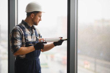 İnşaatçı, inşaat veya yenileme sırasında hava geçirmez yalıtım ve hava korumasını sağlamak için pencere çerçevesine dolgu macunu sürüyor