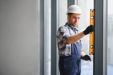 İnşaat ya da yenileme sırasında pencere kurulumunu sağlamak için ruh seviyesini kullanan inşaatçı