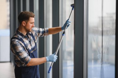 Modern bir ofis binasının camlarını silmek için mavi eldiven giyen temizlikçi.