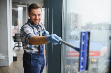 Temizlik işçisi ofis binasının camlarını silmek için cam sileceği kullanır, temiz ve pırıl pırıl bir ortam sağlar.