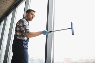Modern bir ofiste cam silmek için mavi eldiven giyen temizlikçi.