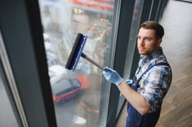 Pencere temizleyicisi mavi eldiven takıyor modern bir binanın camını silmek için cam sileceği kullanıyor.