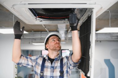 HVC servis teknisyeni havalandırma ünitesini tamir ediyor, başlık ve eldiven takıyor, havalandırmayı ve soğutmayı sağlıyor.