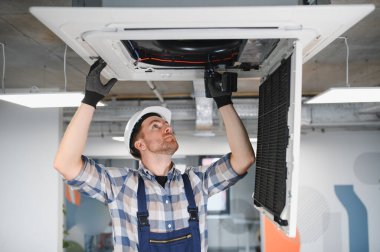 HVC teknisyenleri havalandırma ve soğutmayı sağlamak için tavana monte edilmiş havalandırma ünitesini inceliyor ve onarıyor.