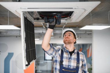 Hvac teknisyeni, kablosuz tornavida kullanıyor, havalandırma sistemi bakımı sırasında havalandırma ünitesi kuruyor.
