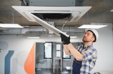 Kask ve eldiven takan Hvac teknisyeni modern bir ofiste klima takıyor veya tamir ediyor