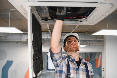Hvac teknisyeni, havalandırma ünitesini tamir ediyor. Kask ve eldiven takıyor, havalandırmayı ve soğutmayı sağlıyor.