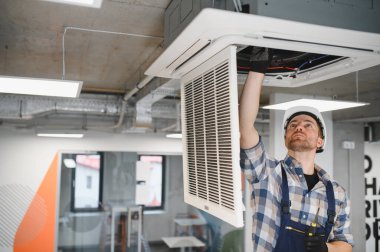 Güvenlik kaskı takan HVC teknisyeni ofis binasına havalandırma sistemi kuruyor.