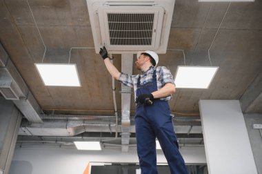 Güvenlik kaskı takan Hvac teknisyeni inşaat halindeki bir binaya havalandırma sistemi kuruyor.