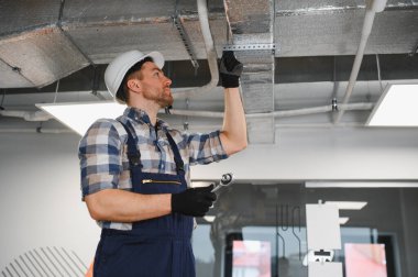 Hvac teknisyeni havalandırma ve havalandırma boruları montajında çalışıyor, güvenlik kaskı takıyor ve aletler kullanıyor.