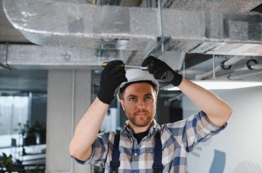 İnşaat halindeki bir binada, güvenlik kaskı takan ve tornavida kullanan profesyonel bir müteahhit.