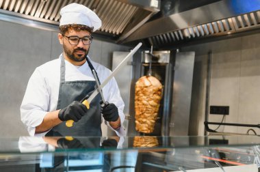 Yemek keskinleştirme bıçağı profesyonel mutfakta dikey rostodan et dilimlemeye hazırlanıyor sokak yemeği hazırlıyor.