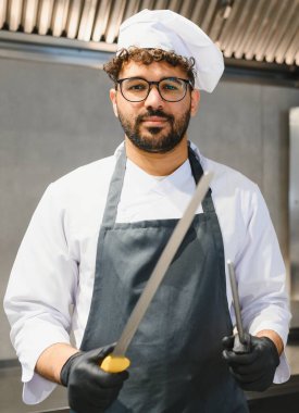 Orta Doğulu şef büyük et bıçağını bileyerek keskin bir çelikle yemek servisine hazırlanıyor.