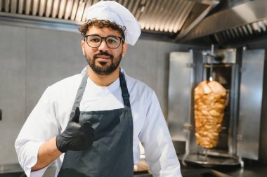 Kendine güvenen bir şef, ticari bir mutfakta düşey bir rosto kullanarak shawarma hazırlarken, uzmanlığını ve kalitesini gösteriyor.