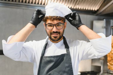 Genç aşçı siyah eldivenler giymiş, şef şapkasını düzeltiyor, gülümsüyor ve lezzetli kebaplar ve shawarmas hazırlıyor.