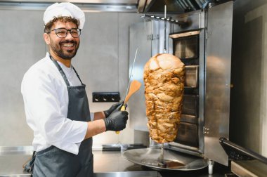 Bir bıçak ve spatula tutarken gülümseyen mutlu aşçı, şavurmayı ustalıkla hazırlıyor.