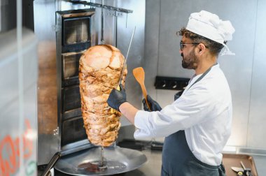 Profesyonel bir şef, ticari bir mutfakta lezzetli shawarma etini dönüşümlü bir tükürükten ustalıkla dilimliyor. Popüler bir sokak yemeği hazırlıyor.