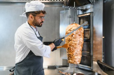 Profesyonel şef döner tükürükten kızartılmış eti ustalıkla dilimliyor, ticari bir mutfakta lezzetli bir shawarma hazırlıyor.
