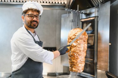 Profesyonel bir aşçı, ticari bir mutfakta düşey tükürükten kebap doğruyor, geleneksel bir shawarma ya da jiroskop hazırlıyor.