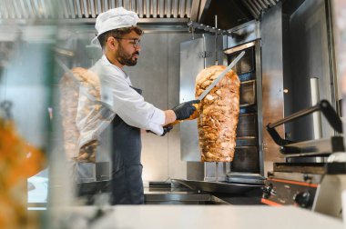 Profesyonel aşçı lezzetli bir shawarma hazırlıyor, ticari mutfakta et doğruyor, aşçılık uzmanlığı ve sokak yemekleri hazırlıyor.