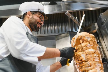 Profesyonel bir şef, ticari bir mutfakta lezzetli shawarma etini dönüşümlü bir tükürükten ustalıkla dilimliyor. Popüler bir sokak yemeği hazırlıyor.