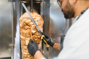 Profesyonel şef baharatlı shawarma etini dönüşümlü tükürükten ustalıkla dilimliyor. Popüler bir orta doğu sokak yemeği hazırlıyor.