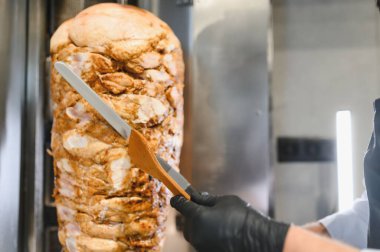 Büyük bıçak ve ahşap spatula kullanarak aşçı, dikey rostodan ince et parçaları dilimlemek, geleneksel shawarma hazırlamak