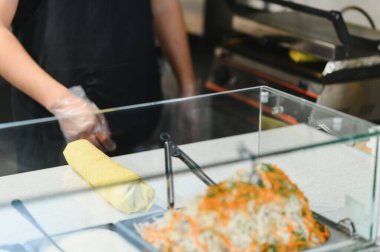 Aşçı bir fast food restoranında et ve sebzelerle sarma yapıyor, yemek güvenliği için eldiven kullanıyor.