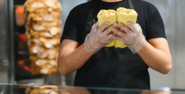 Aşçı, arka planda kebap yapan bir lokantada servis yapmaya hazır iki yeni pişmiş shawarma 'yı gösteriyor.
