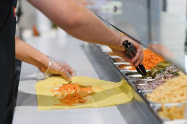 Aşçı Shawarma 'ya salatalık turşusu ve havuç ekliyor maşa kullanıyor, doğu mutfağında özel bir fast food restoranında çalışıyor.