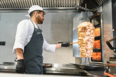 Profesyonel bir aşçı döner vaziyette et doğruyor, leziz bir shawarma hazırlıyor ya da ticari bir mutfakta kebap yapıyor.