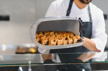 Profesyonel aşçı ticari bir mutfakta lezzetli bir tepsi baklava hamur işi sunuyor. Orta doğu ya da Akdeniz mutfağında uzmanlık gösteriyor.