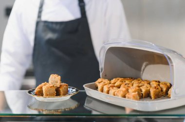 Taze yapılmış baklava, geleneksel bir ortadoğu tatlısı, tezgahta sergileniyor, arka planda bir şef var, servis yapmaya hazır.