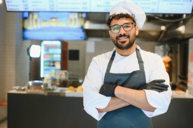 Üniformalı, siyah eldivenli, kollarını kavuşturup, kebap lokantasının mutfağında gülümseyen kendine güvenen profesyonel bir şef.