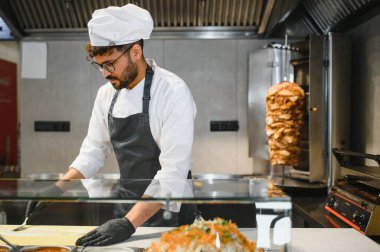 Profesyonel aşçı pide ekmeğine sos sürüyor, ticari bir mutfakta taze malzemeler kullanarak lezzetli bir donör kebabı hazırlıyor.