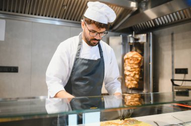 Profesyonel bir aşçı fast food restoranının mutfağında lezzetli shawarma ve kebaplar hazırlıyor, sokak yemeklerinin sanatını sergiliyor.