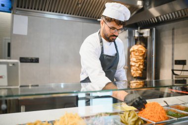 Orta Doğulu şef diğer taze malzemelere rendelenmiş havuç eklerken bir fast food restoranında donör kebap ya da shawarma hazırlıyor.