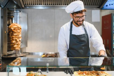 Siyah eldiven giyen genç aşçı hızlı bir fast food restoranında lezzetli bir donör kebabı hazırlıyor.