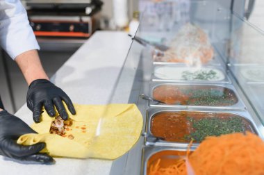 Aşçı lavaş ekmeğine et ve sos ekler, fast food restoranında donör kebap ya da shawarma yapar.