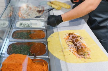 Aşçı, et, sebze ve çeşitli malzemelerle shawarma ambalajına sos ekliyor.