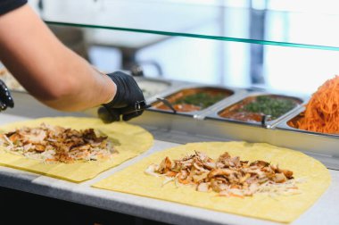 Doğu mutfağında uzmanlaşmış bir fast food restoranında lezzetli bir shawarma ya da kebap hazırlamak için lavaşın üzerine tavuk ve sebze ekliyorum.