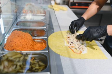 Profesyonel bir mutfakta, üniforma ve eldiven giyerek shawarma ya da donör kebabı için dönen bir tükürükten et dilimleyen Ortadoğulu şef.