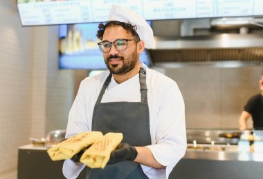 Siyah eldiven giyen Arap şef, doğu mutfağında uzmanlaşmış bir fast food restoranında üç kebap tutuyor.