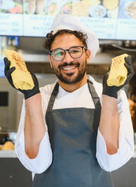 Bir sokak restoranında siyah eldiven ve önlük giymiş iki lezzetli şwarma gösteren mutlu bir aşçı.