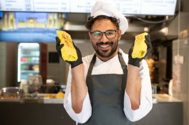 Siyah eldiven giyip elinde iki lezzetli shawarma tutarak fast food restoranında poz veren mutlu bir aşçı.