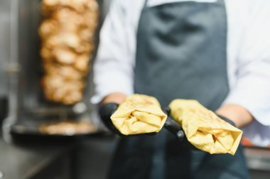 Siyah eldiven giyen aşçı arka planda dikey bir rostoda pişirilmiş etli iki lezzetli shawarma sunar.