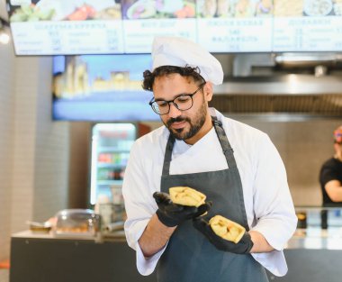 Üniforma giyen profesyonel şef ve eldivenler ticari bir mutfakta iki Shawarma 'yı dikkatle inceliyor. Müşterilere birinci sınıf kalite ve zevk sağlıyor.