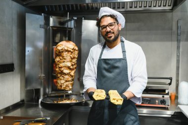 Siyah eldiven ve önlük takan aşçı bir fast food restoranında donör kebabının yanında iki shawarma tutuyor.